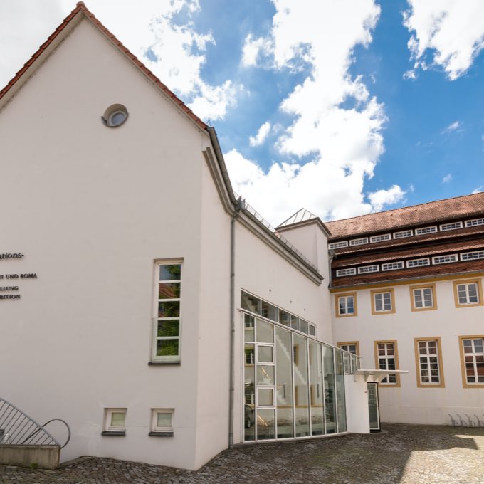 Blick in den Innenhof des Dokumentations- und Kulturzentrums Deutscher Sinti und Roma. Zu sehen ist der Eingangsbereich mit einer großen Glasfassade. - zur Website des Zentralrats
